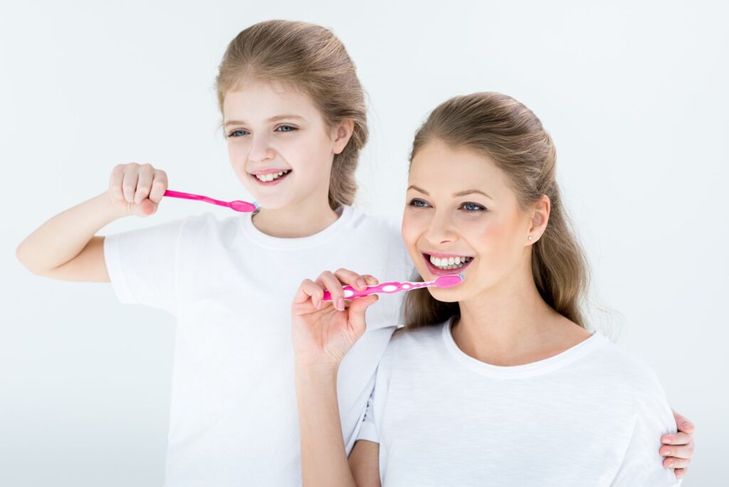 Happy mother and daughter cleaning teeth with toothbrushes on white